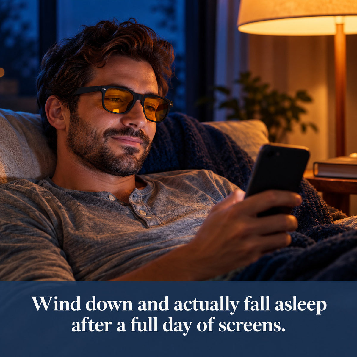 Man relaxing on the couch at night, scrolling his phone while wearing Plemea Retro Night amber glasses